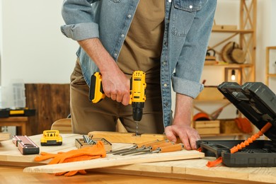 Photo of Craftsman working with drill at wooden table in workshop, closeup