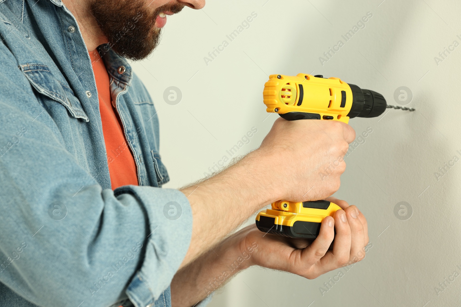 Photo of Smiling man drilling white wall at home, closeup