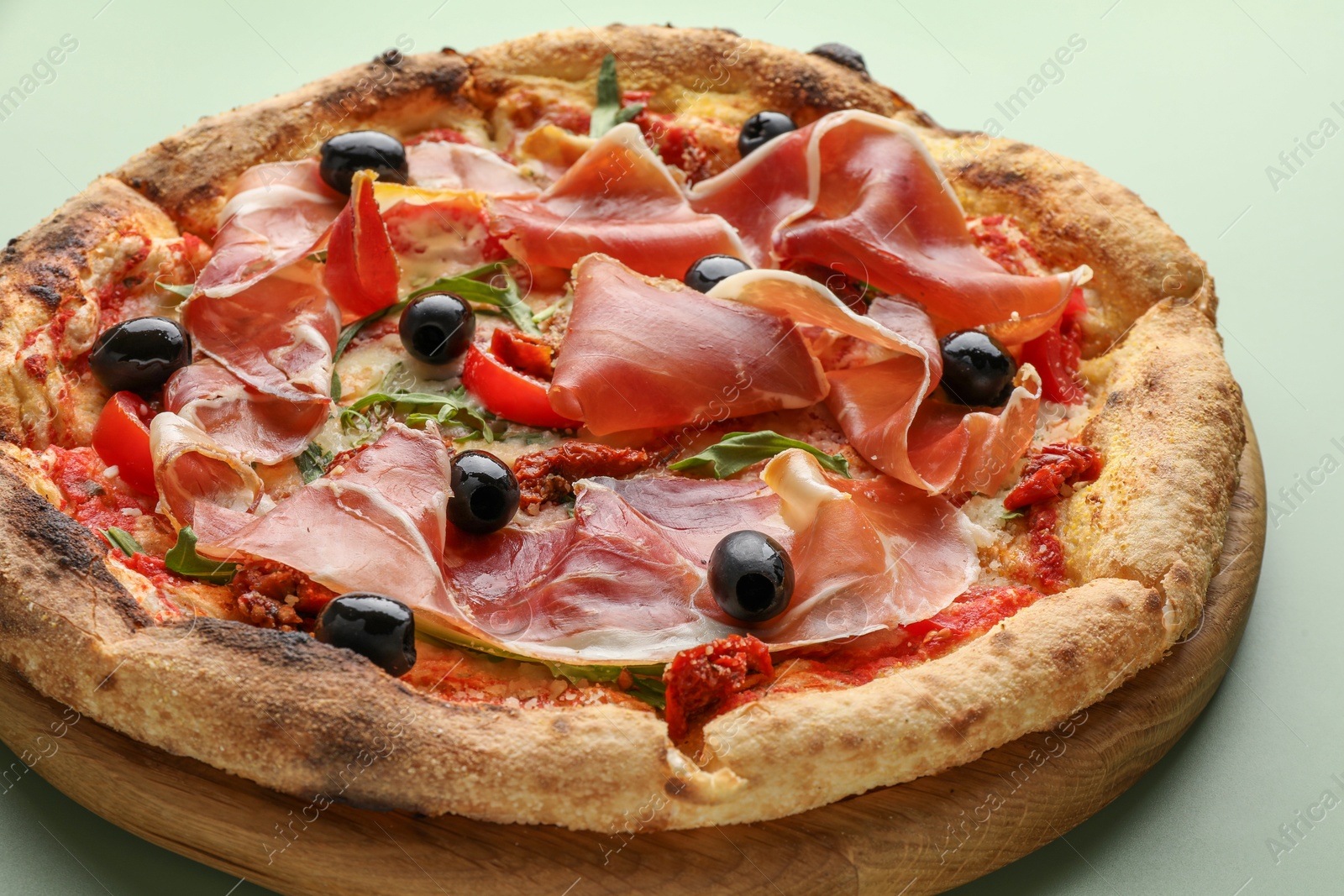 Photo of Tasty pizza with cured ham, olives and sun-dried tomato on green background, closeup