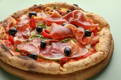 Photo of Tasty pizza with cured ham, olives and sun-dried tomato on green background, closeup