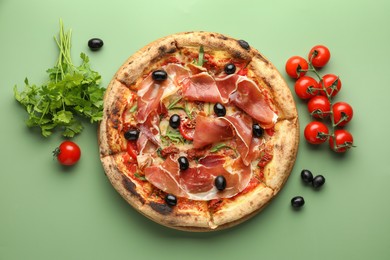 Photo of Tasty pizza with cured ham, olives, tomatoes and parsley on green background, top view