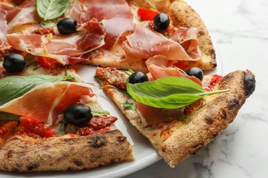 Photo of Tasty pizza with cured ham, olives, sun-dried tomato and basil on white marble table, closeup