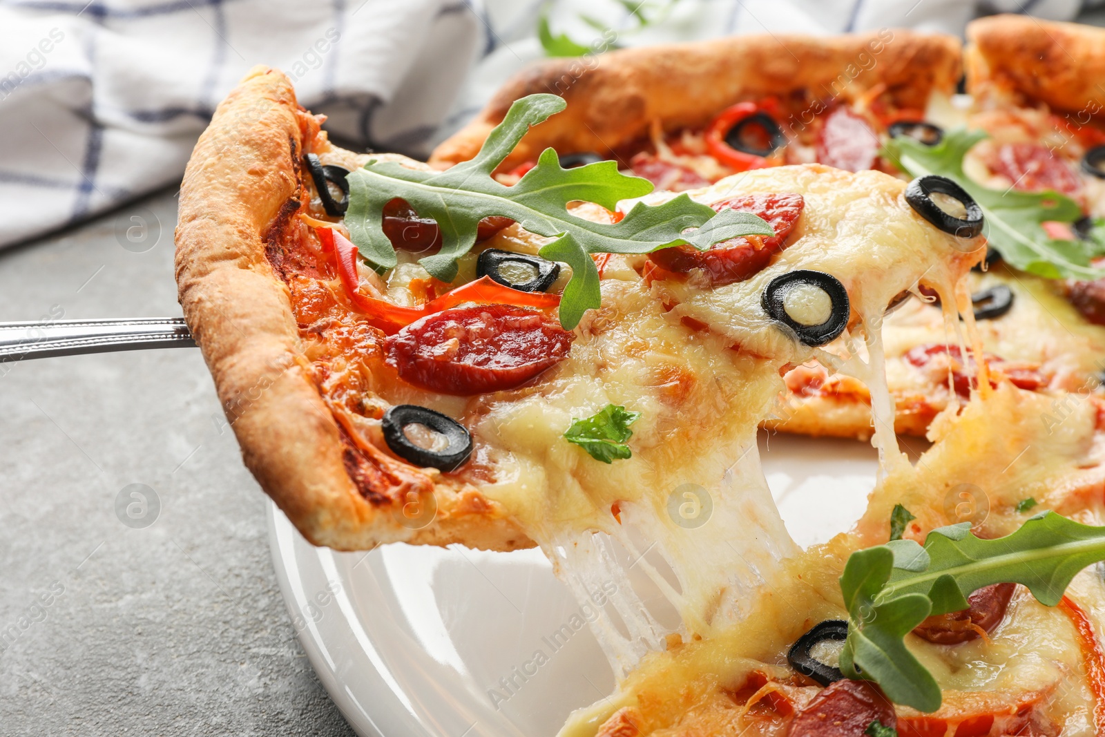 Photo of Taking piece of tasty pizza with smoked sausages, olives, pepper and parsley at gray table, closeup