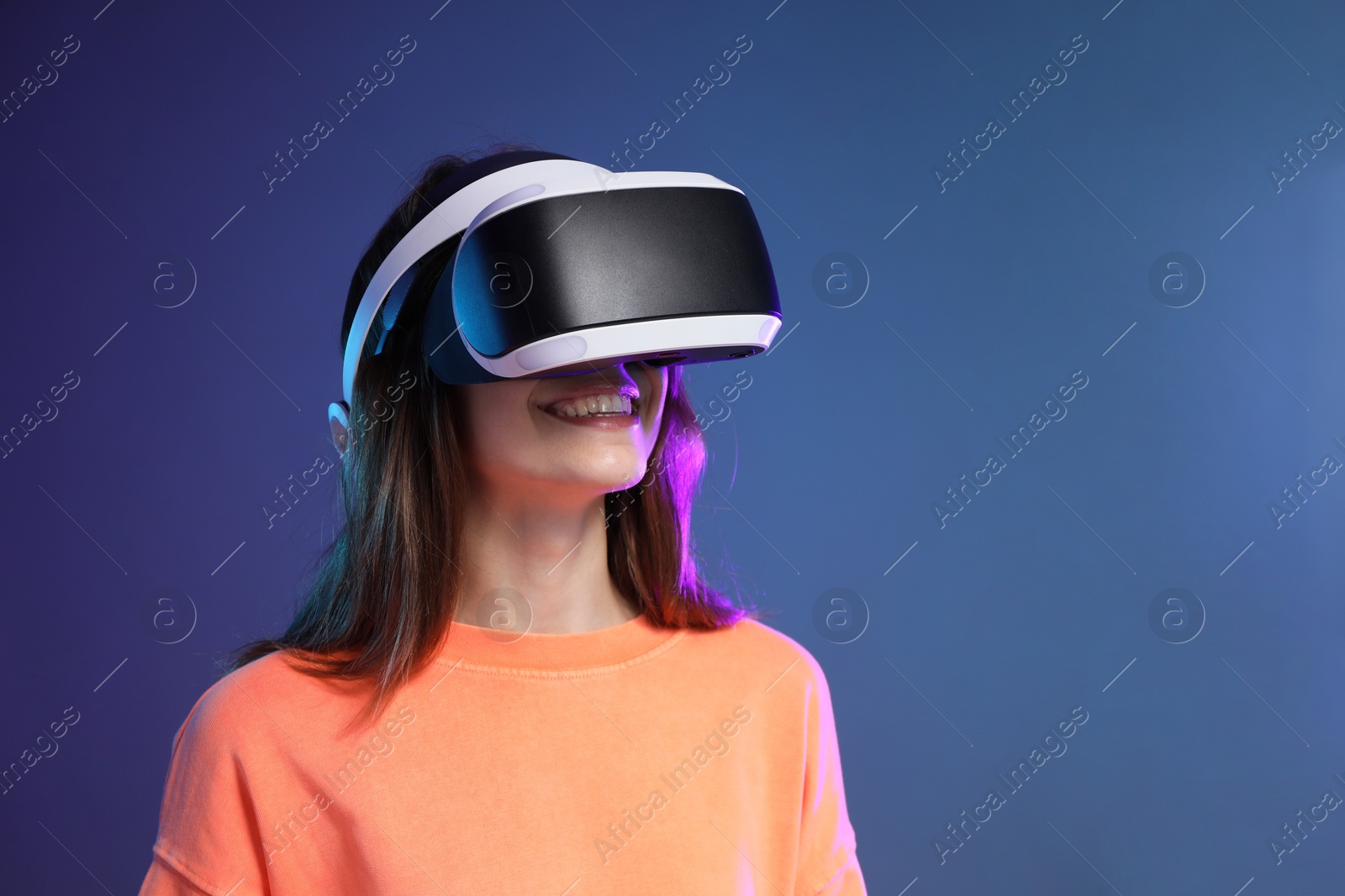 Photo of Smiling woman using virtual reality headset on dark blue background. Space for text