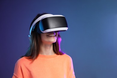 Photo of Smiling woman using virtual reality headset on dark blue background. Space for text