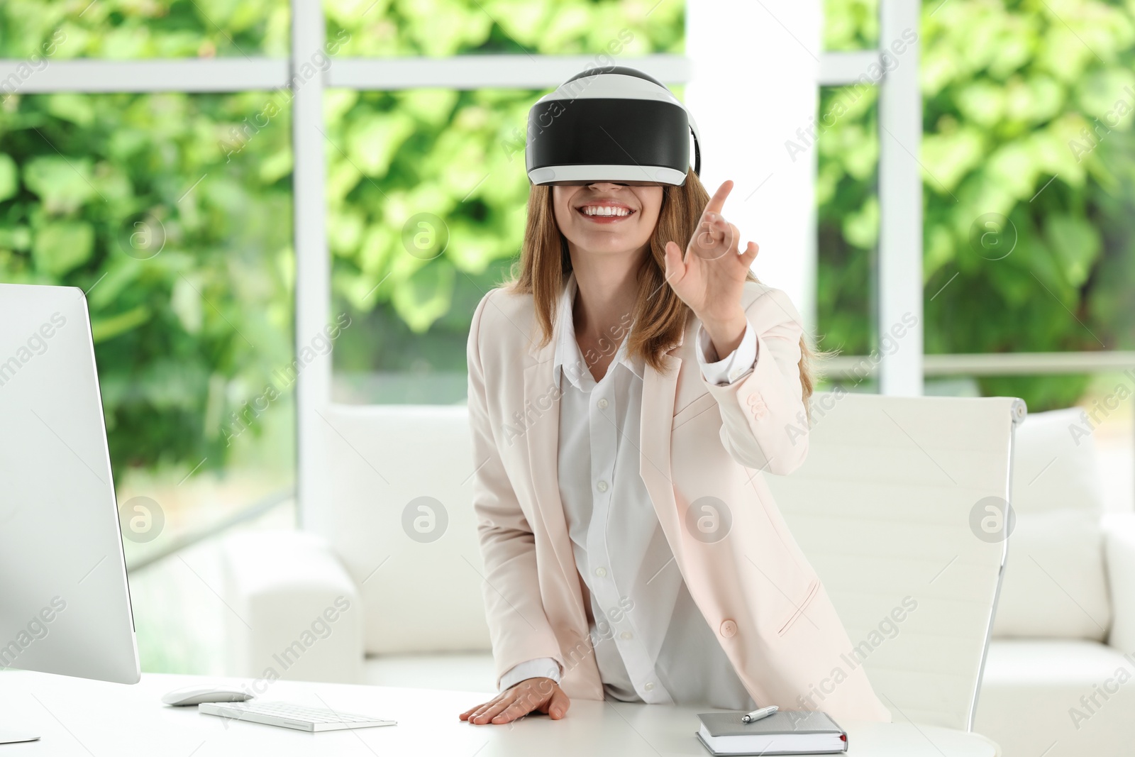 Photo of Smiling woman using virtual reality headset at workplace in office