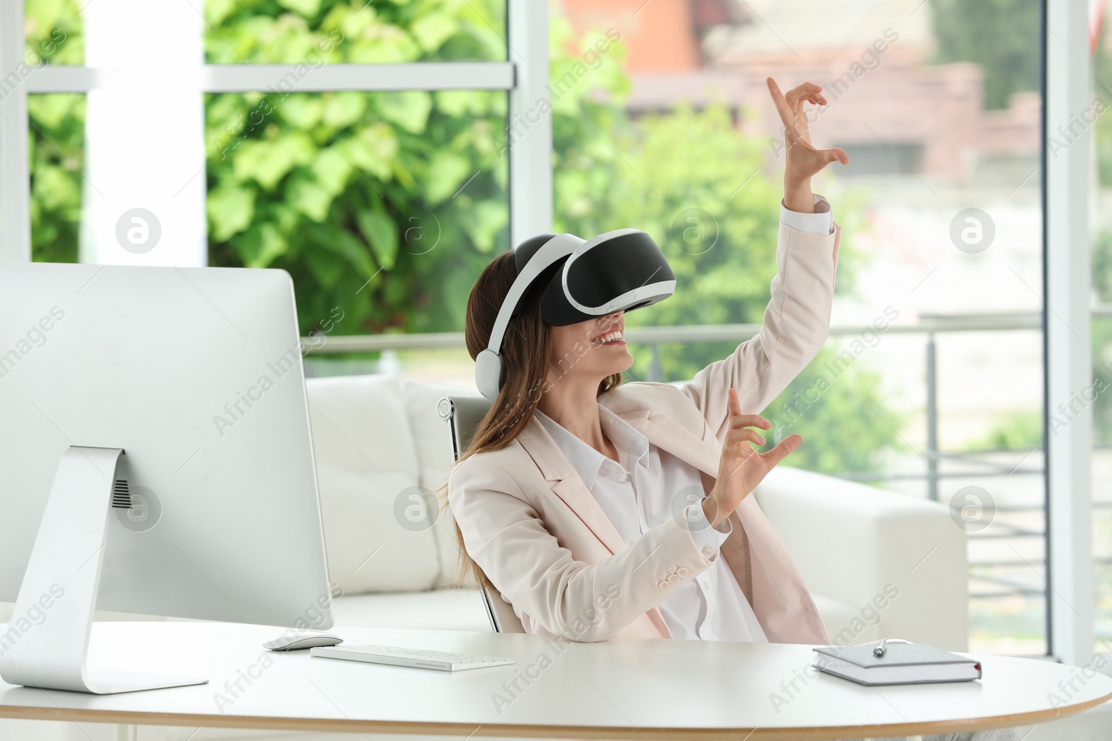 Photo of Smiling woman using virtual reality headset at workplace in office