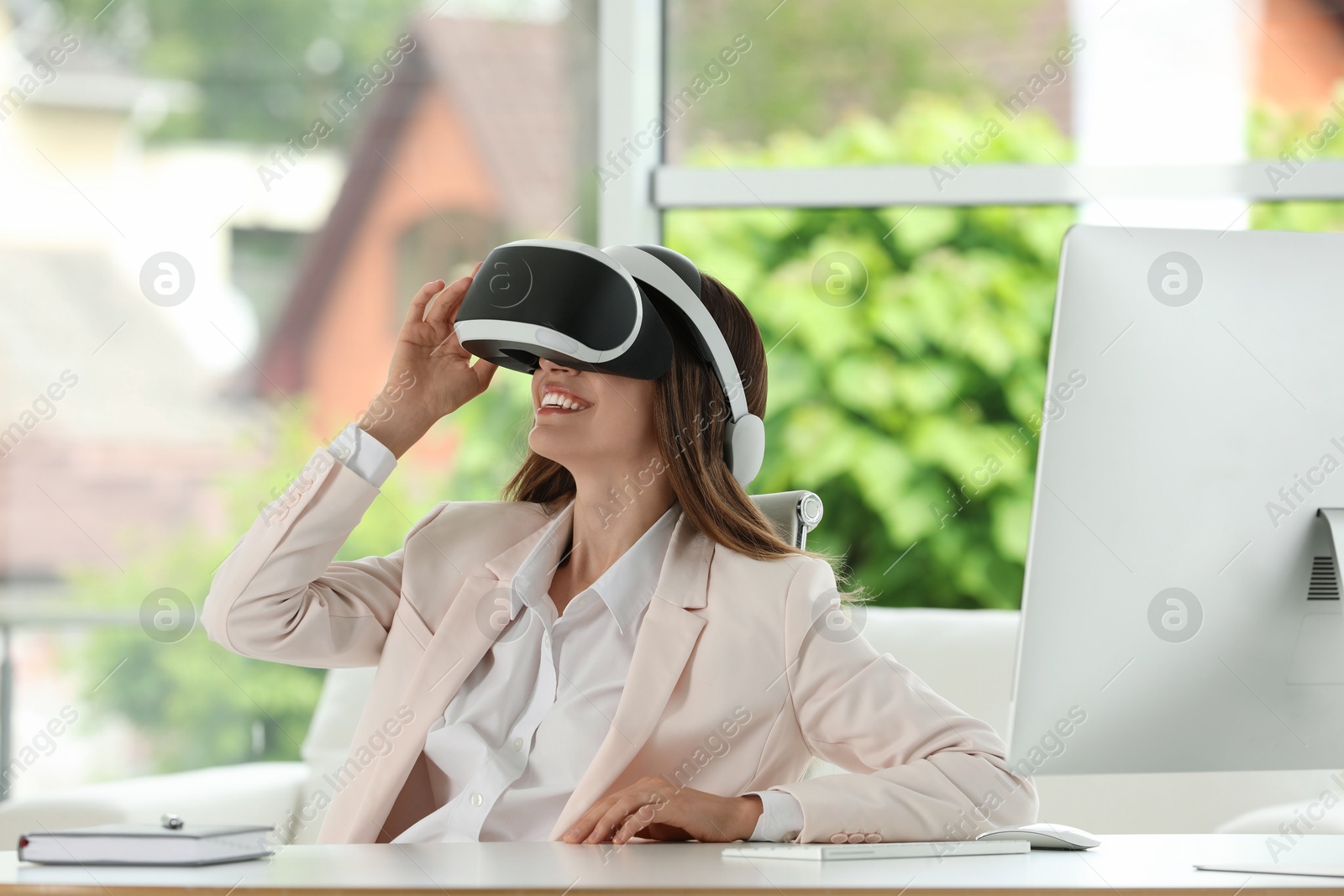 Photo of Smiling woman using virtual reality headset at workplace in office