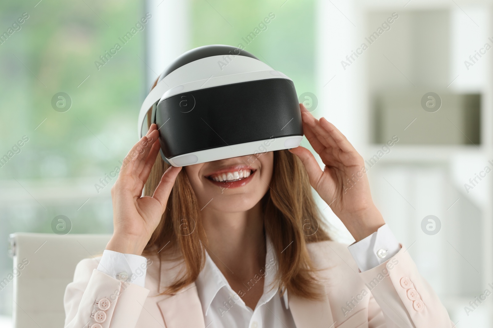 Photo of Smiling woman using virtual reality headset in office