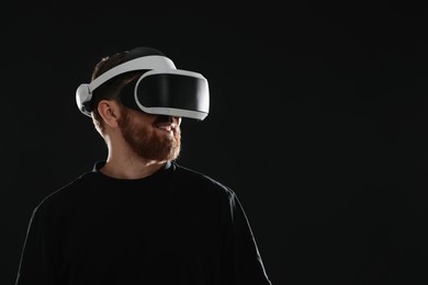 Photo of Man using virtual reality headset on black background. Space for text