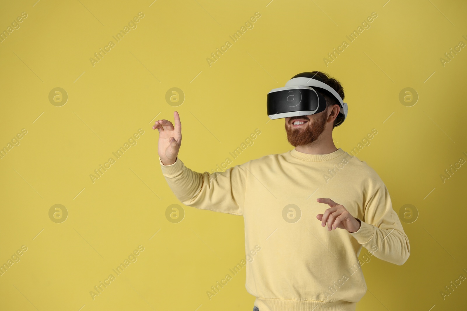 Photo of Happy man using virtual reality headset on pale yellow background. Space for text