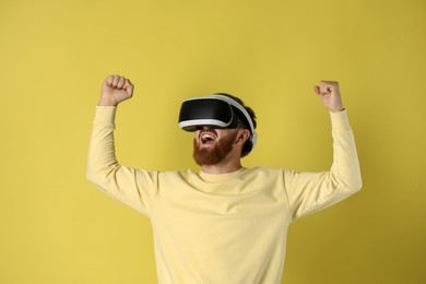 Photo of Emotional man using virtual reality headset on pale yellow background