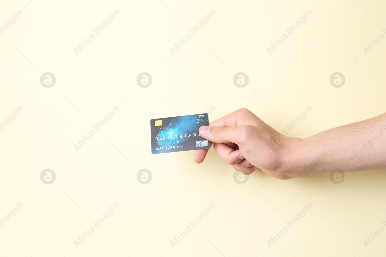 Photo of Man holding credit card on pale yellow background, closeup