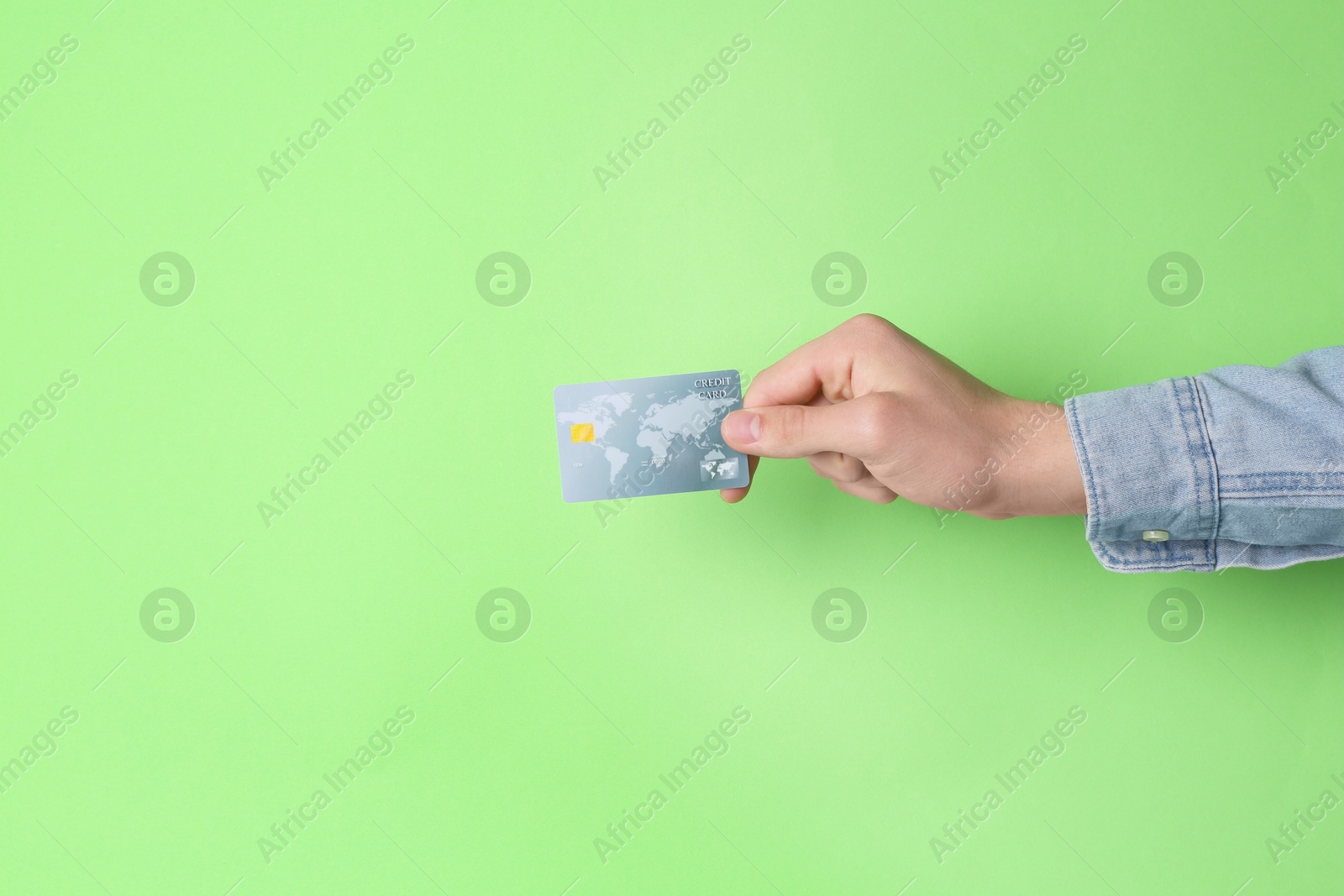 Photo of Man holding credit card on light green background, closeup