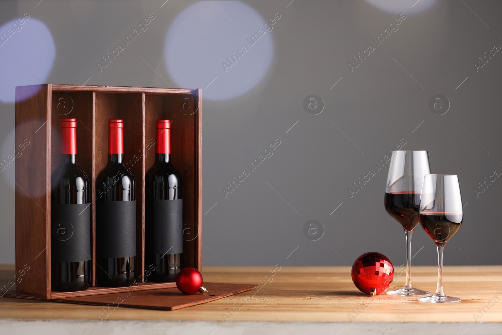 Photo of Wooden gift box with bottles of wine, glasses and red Christmas balls on table, space for text