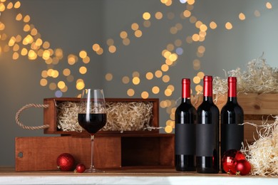 Photo of Bottles of wine, glass, wooden gift boxes and red Christmas balls on table