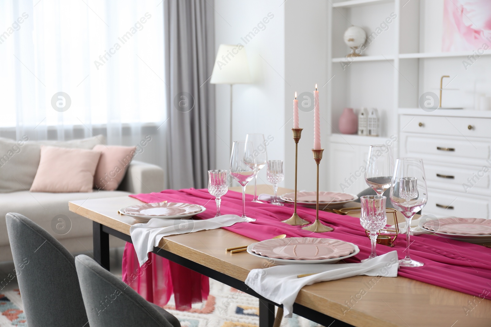 Photo of Beautiful table setting with burning candles and pink accent in dining room