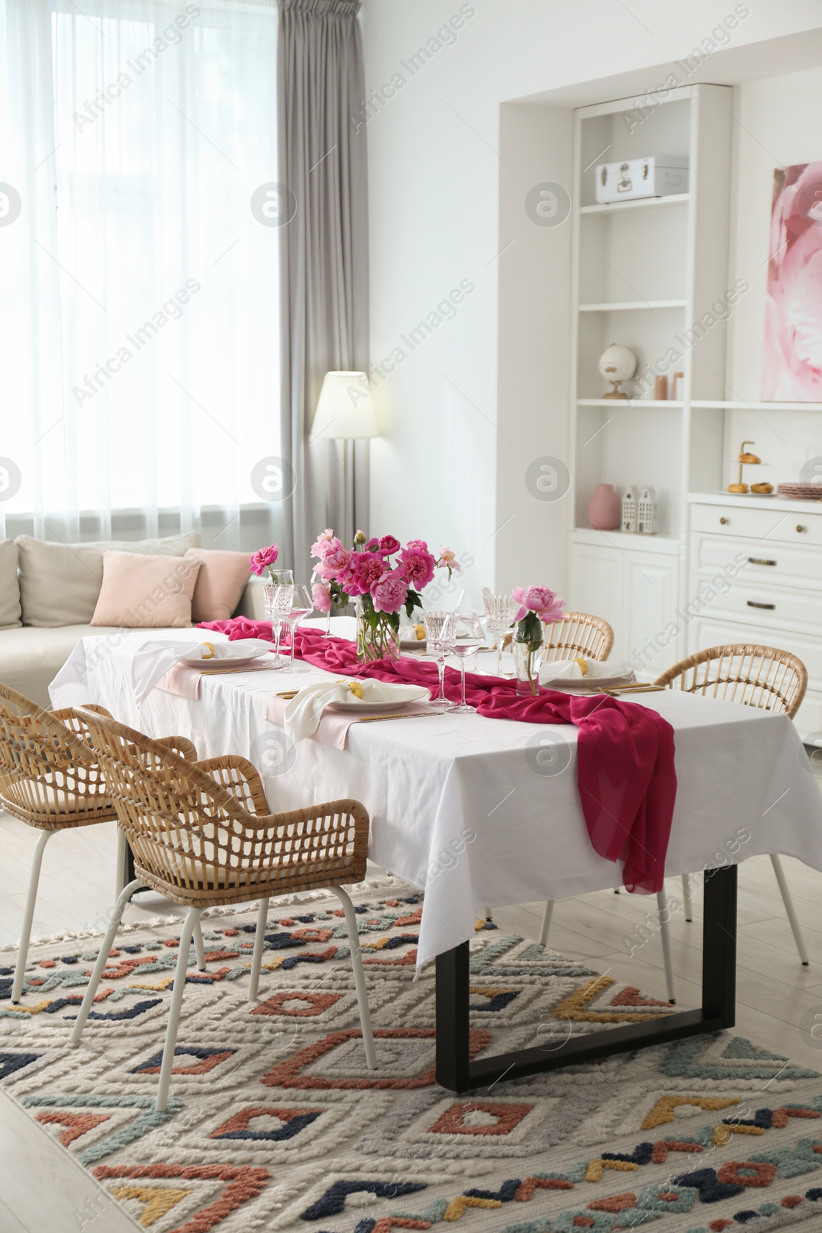 Photo of Beautiful table setting with pink accent and rattan chairs in dining room