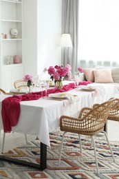 Photo of Beautiful table setting with pink accent and rattan chairs in dining room