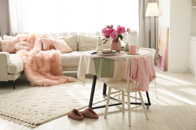 Photo of Pink peonies on table, chair and sofa in living room