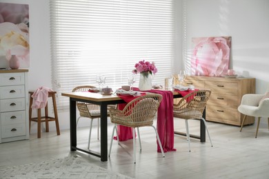 Photo of Pink peonies on table with beautiful setting and rattan chairs in dining room