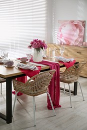 Photo of Pink peonies on table with beautiful setting and rattan chairs in dining room