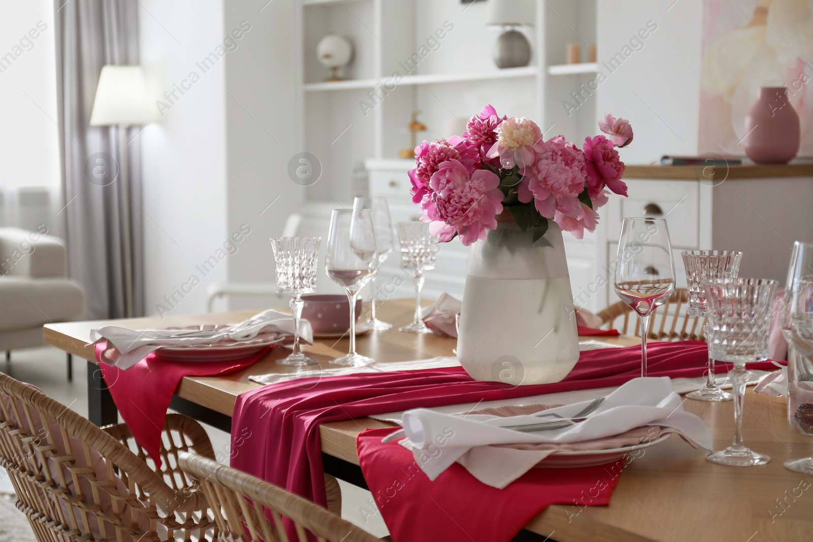 Photo of Pink peonies on table with beautiful setting and rattan chairs in dining room