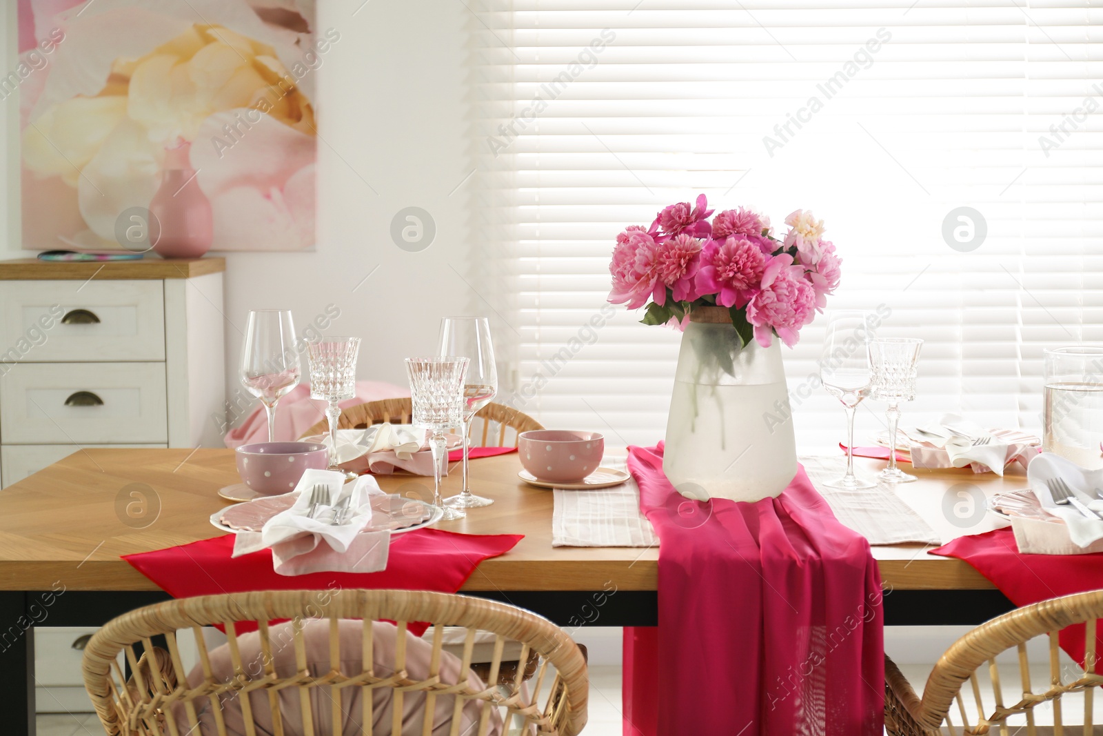 Photo of Pink peonies on table with beautiful setting and rattan chairs in dining room