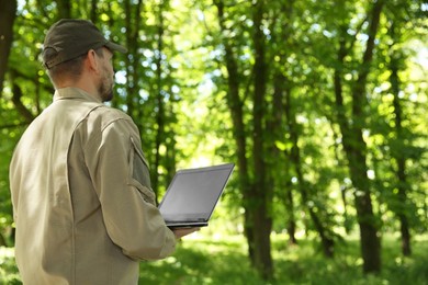 Photo of Forester with laptop examining plants in forest, back view. Space for text