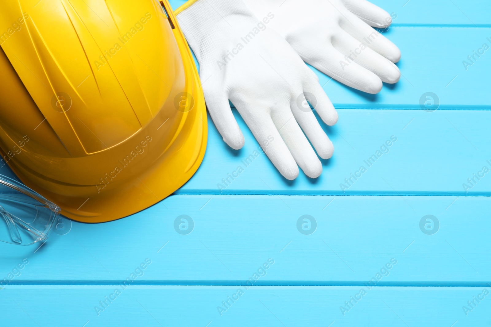 Photo of Hard hat, protective gloves and goggles on light blue wooden background, flat lay. Space for text
