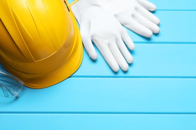 Photo of Hard hat, protective gloves and goggles on light blue wooden background, flat lay. Space for text