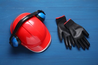 Photo of Hard hat, protective gloves and earmuffs on blue wooden background, flat lay