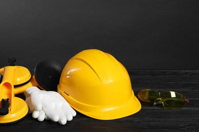 Photo of Hard hat, suction lifters, protective gloves and goggles on black wooden surface against gray background