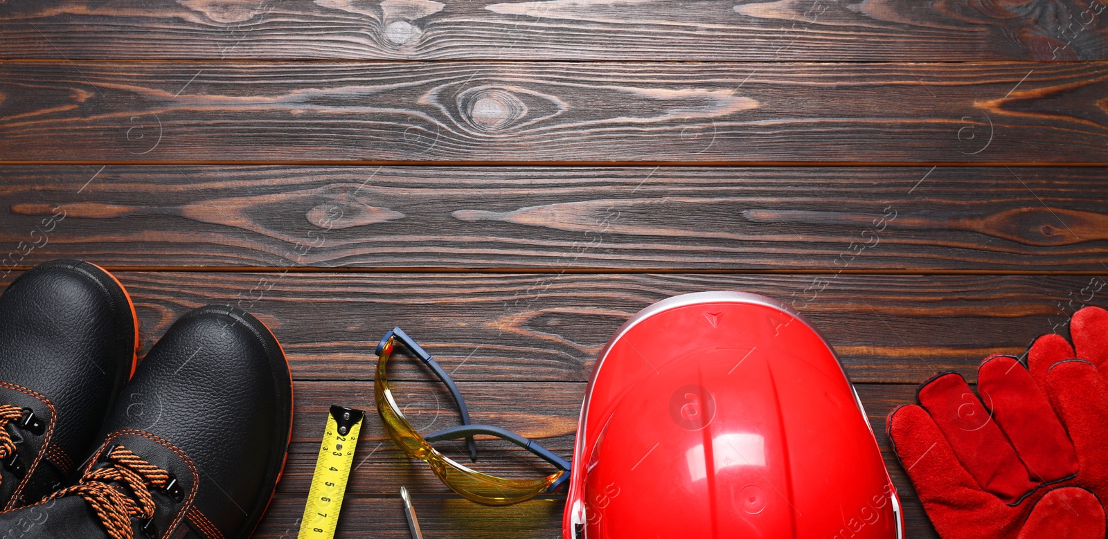 Photo of Pair of working boots, hard hat, protective gloves, goggles and tape measure on wooden background, flat lay. Space for text