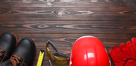 Photo of Pair of working boots, hard hat, protective gloves, goggles and tape measure on wooden background, flat lay. Space for text