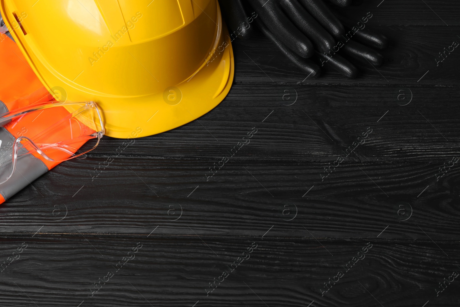 Photo of Reflective vest, hard hat, protective gloves and goggles on black wooden background, above view. Space for text