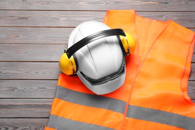 Photo of Reflective vest, hard hat, earmuffs and goggles on wooden background, top view. Space for text