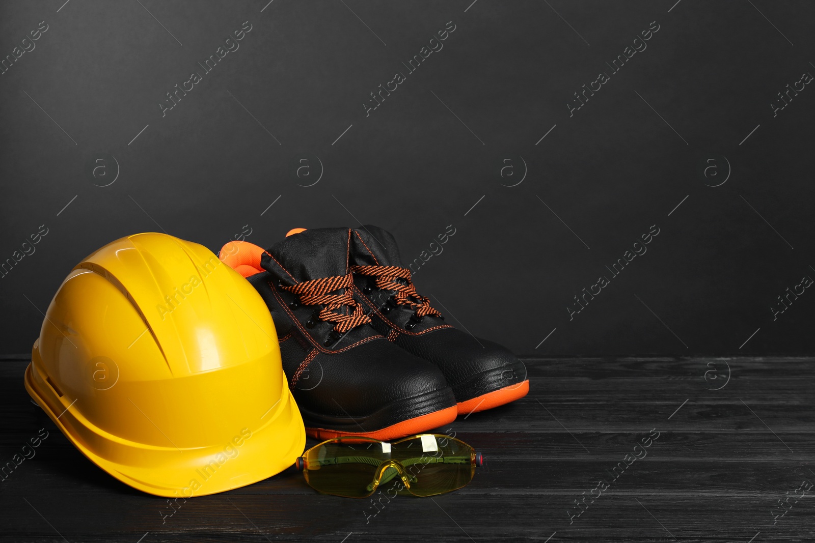 Photo of Pair of working boots, hard hat and goggles on black wooden surface, space for text