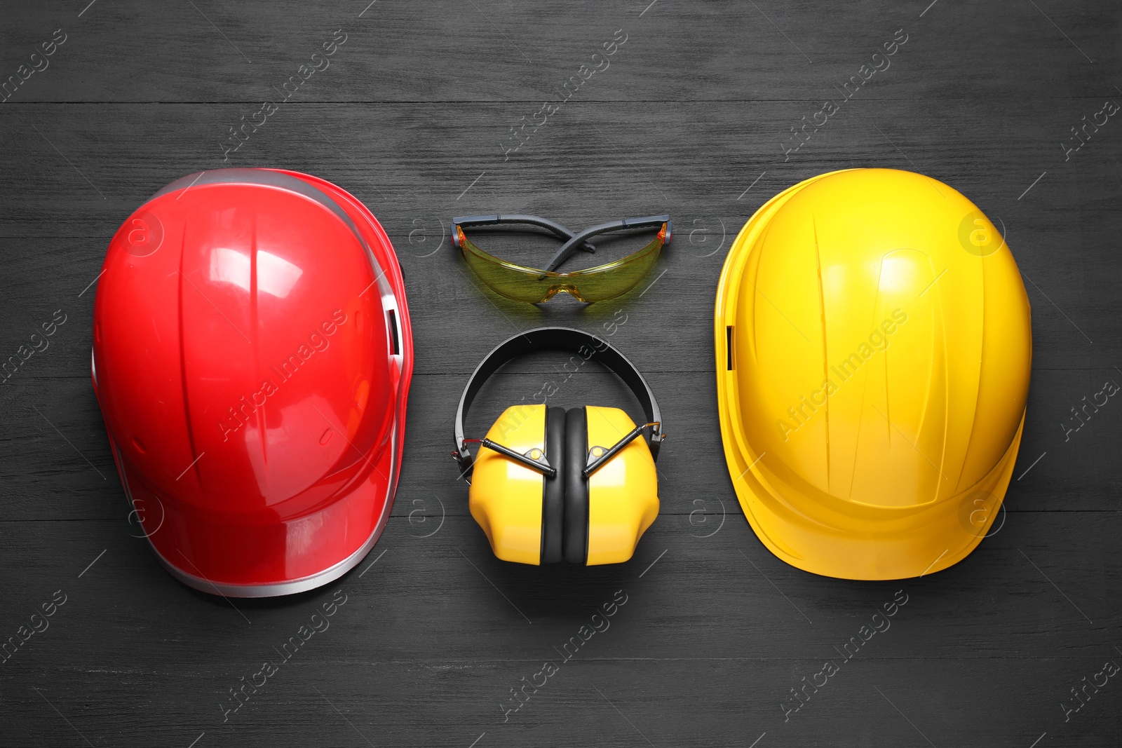 Photo of Hard hats, earmuffs and goggles on black wooden background, flat lay