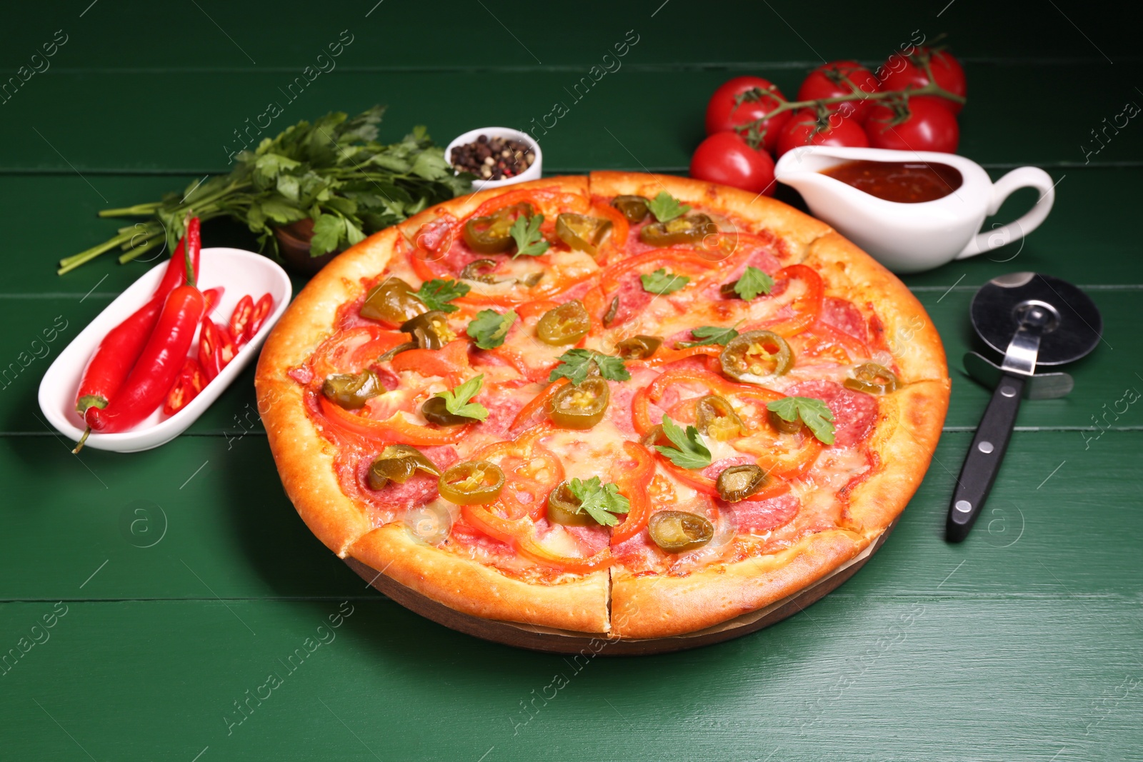 Photo of Delicious pizza Diablo, ingredients and cutter on green wooden table