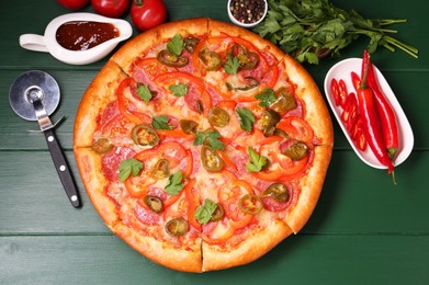 Photo of Delicious pizza Diablo, ingredients and cutter on green wooden table, flat lay