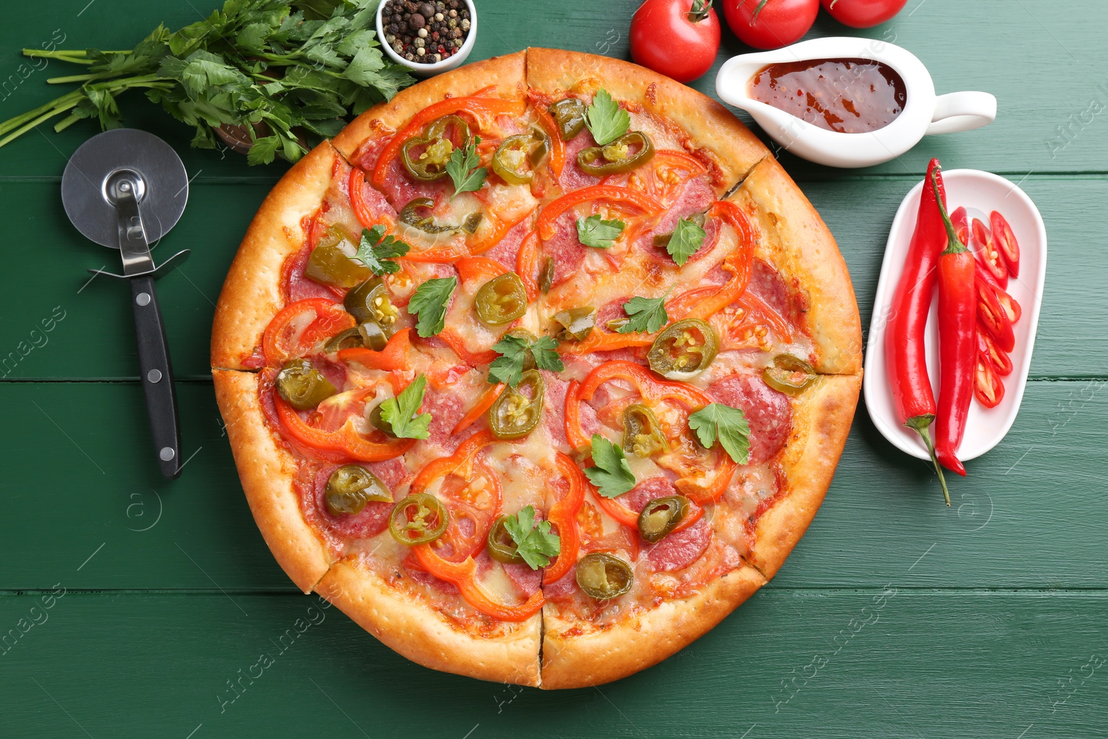 Photo of Delicious pizza Diablo, ingredients and cutter on green wooden table, flat lay