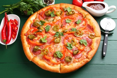 Photo of Delicious pizza Diablo, ingredients and cutter on green wooden table