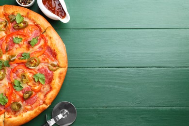 Photo of Delicious pizza Diablo, sauce and cutter on green wooden table, flat lay. Space for text