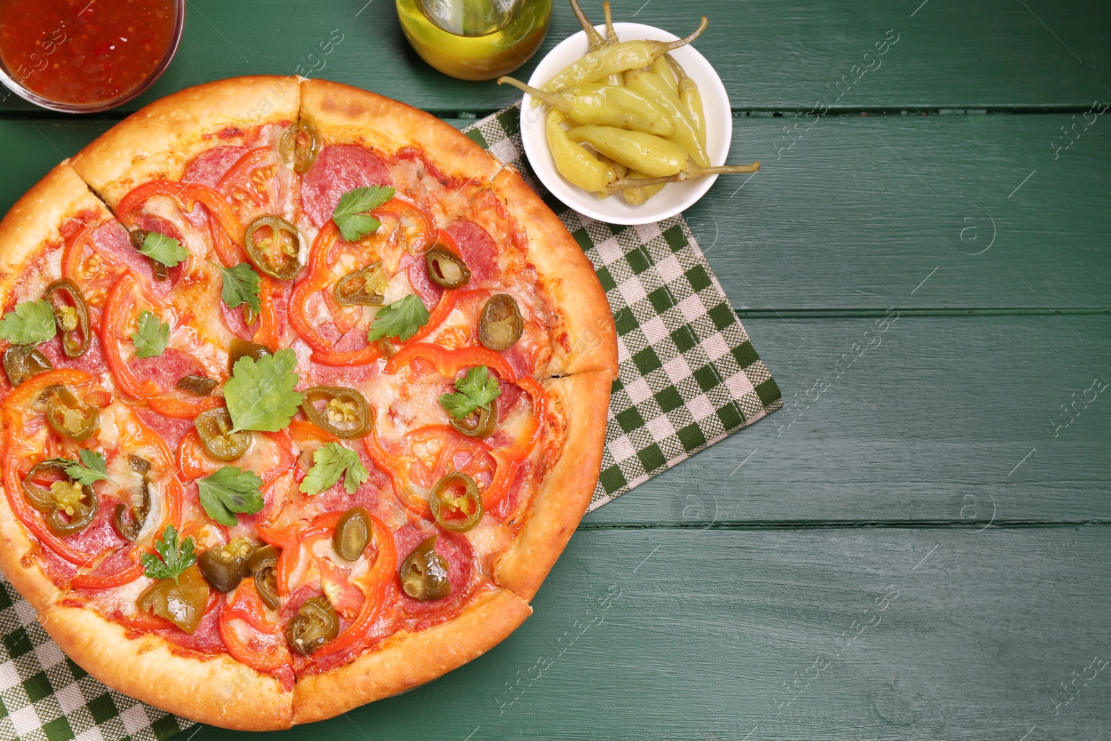 Photo of Delicious pizza Diablo and ingredients on green wooden table, flat lay. Space for text