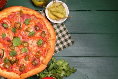 Photo of Delicious pizza Diablo and ingredients on green wooden table, flat lay. Space for text