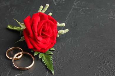 Photo of Stylish red boutonniere and rings on black table, space for text