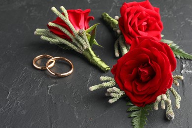 Photo of Many stylish red boutonnieres and rings on black table