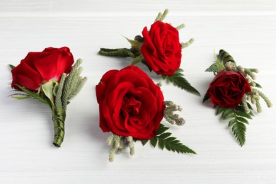 Photo of Many stylish red boutonnieres on white wooden table