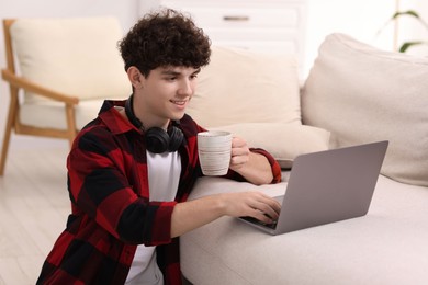 Photo of Teenager with cup of drink working on laptop at home. Remote job